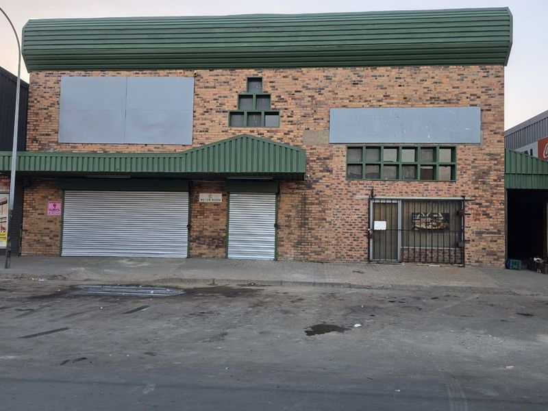 Industrial building facade featuring brick construction, metal roller shutter doors, and secure access points, suitable for commercial or warehouse operations.