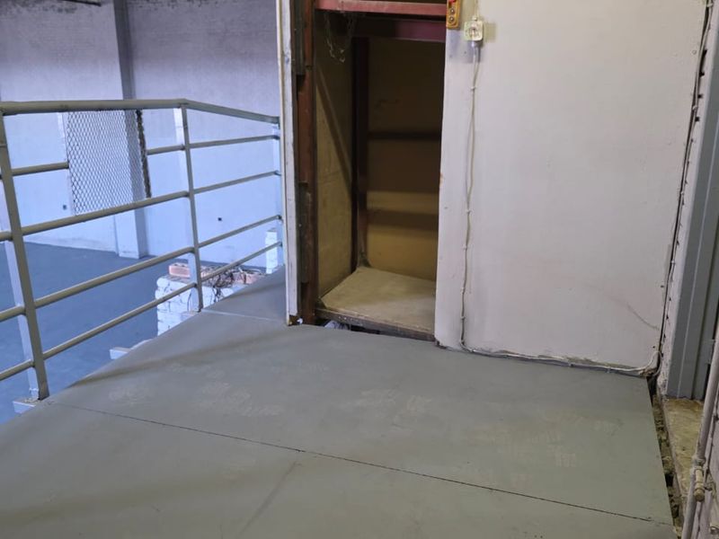 Industrial mezzanine level featuring a freight lift, metal safety railing, and exposed steel roof structure, suitable for storage or operational use.