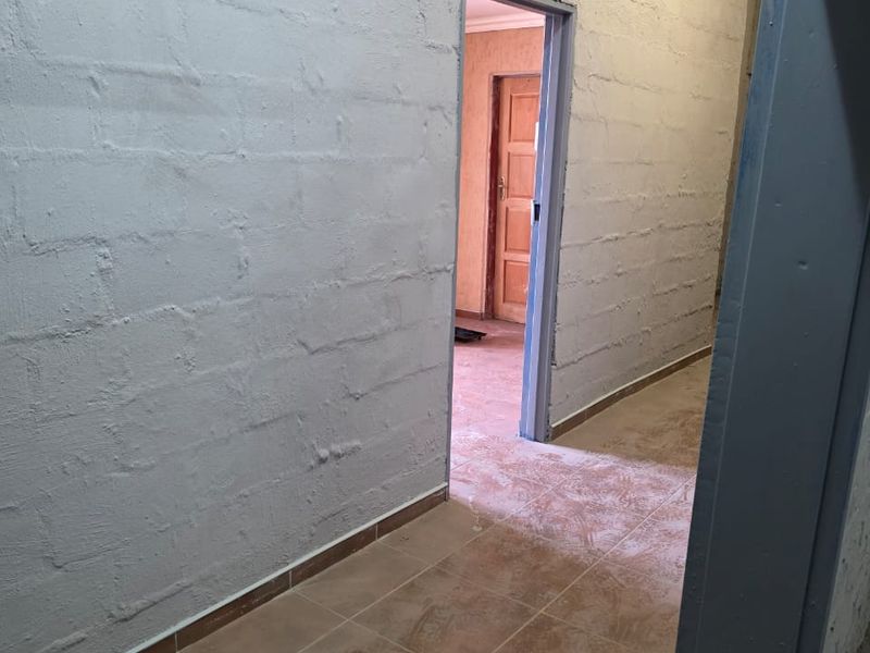 A functional hallway featuring tiled flooring and painted concrete block walls, leading into an adjacent room with a timber door.