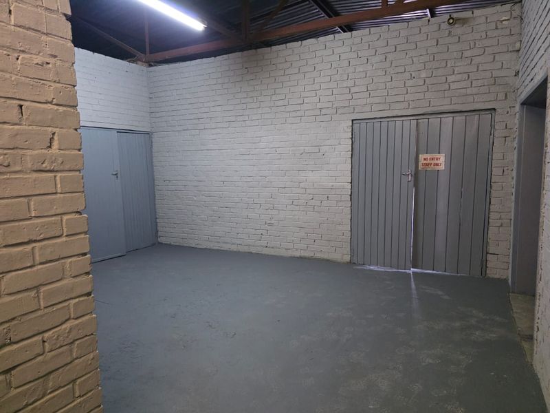 An empty industrial utility space featuring exposed brick walls, painted concrete flooring, and exposed roof trusses with overhead fluorescent lighting.