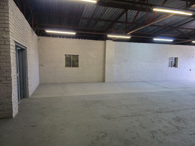 Spacious industrial utility area featuring painted brick walls, exposed steel roof trusses, fluorescent lighting, and a durable concrete floor.