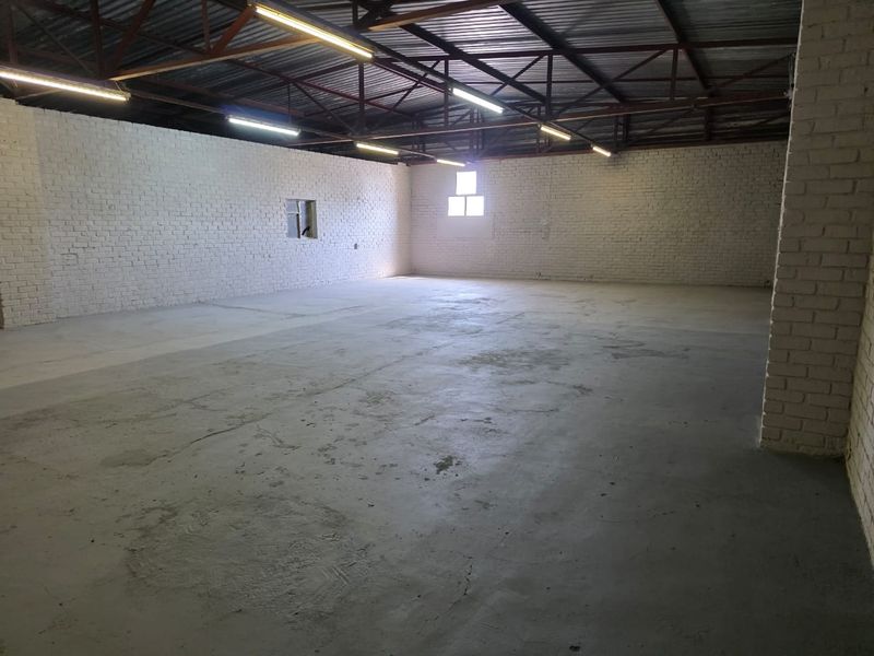 Spacious industrial utility area featuring exposed steel roof trusses, painted brick walls, and durable concrete flooring with overhead strip lighting.