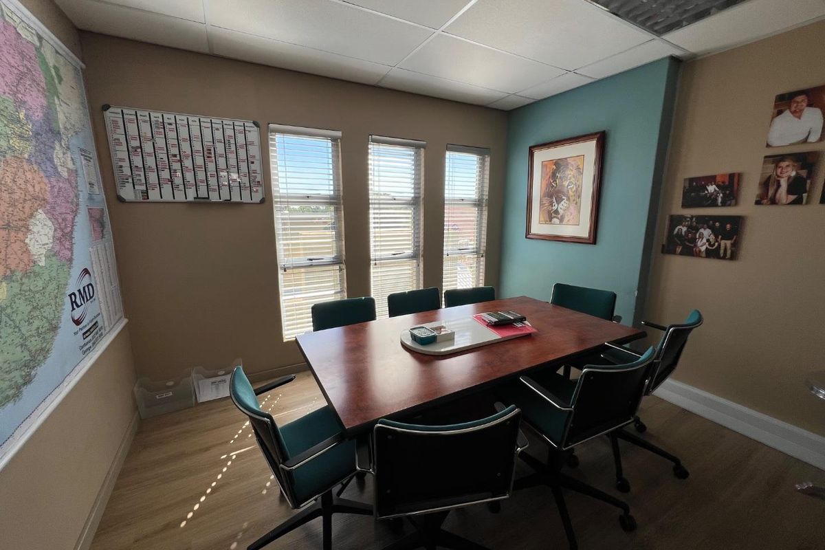 A functional commercial office space featuring wood-look flooring, suspended ceiling tiles, and large windows providing natural light.