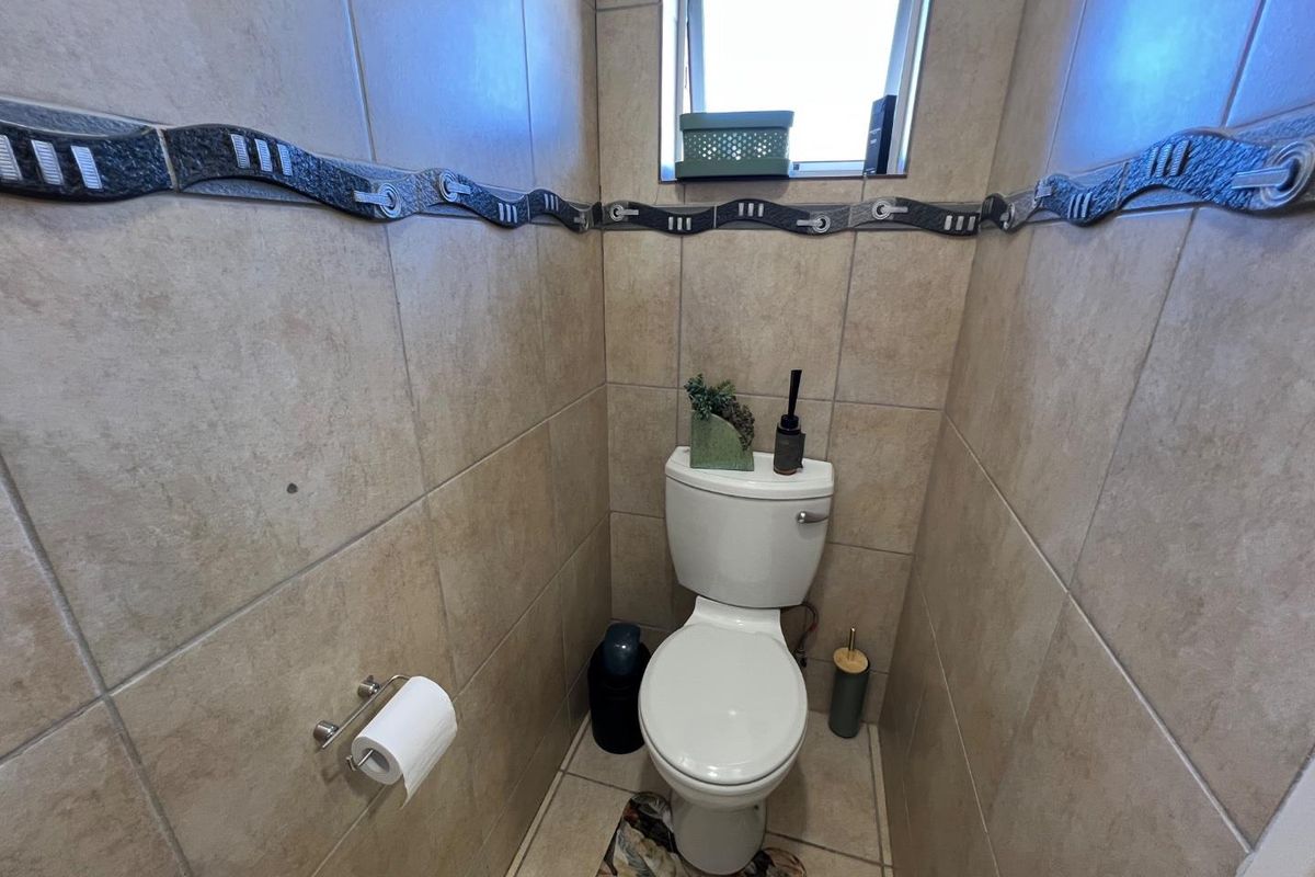 A compact guest bathroom featuring floor-to-ceiling ceramic tiling, a decorative accent border, and a standard white toilet suite.