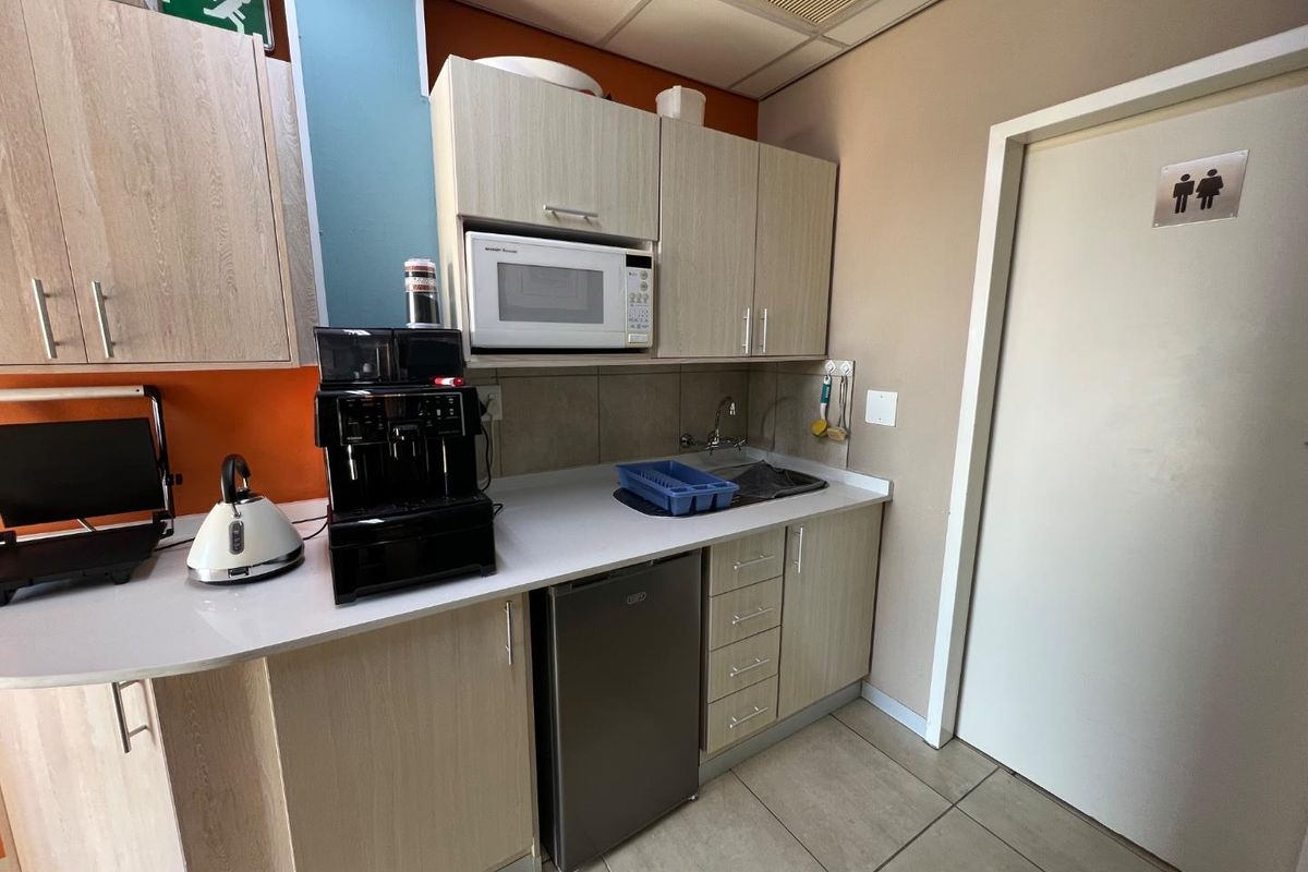 Compact commercial kitchenette featuring light wood cabinetry, built-in microwave, under-counter fridge, and a stainless steel sink.
