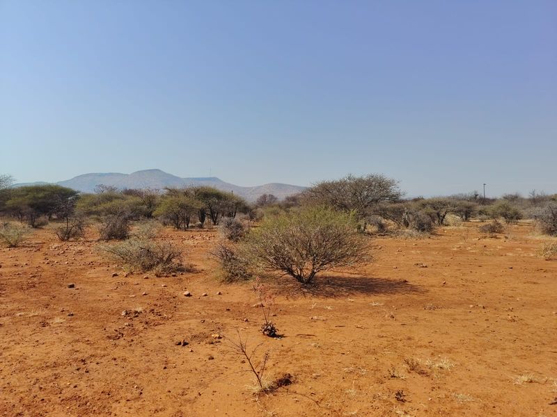A wide-angle view of the vacant commercial land featuring natural arid terrain, native shrubs, and a scenic mountain range in the distance.
