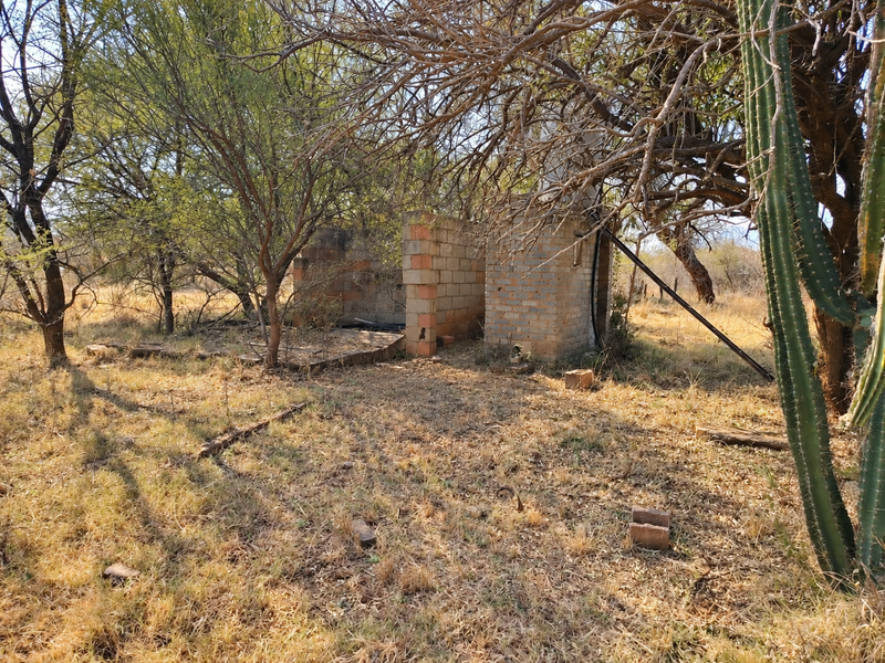 A view of an incomplete brick masonry structure situated on a vacant commercial plot, surrounded by natural vegetation and trees.