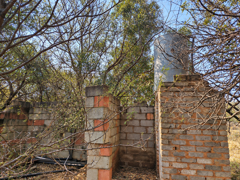 An outdoor utility area featuring concrete block masonry walls, an elevated water storage tank, and exposed plumbing infrastructure surrounded by overgrown trees.