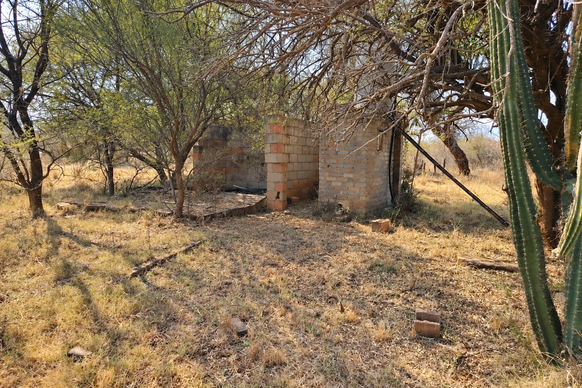 A view of an incomplete brick masonry structure situated on a vacant commercial plot, surrounded by natural vegetation and trees.