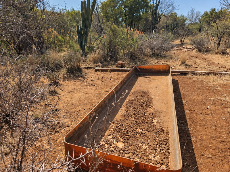 A view of a vacant commercial land plot featuring a weathered metal water trough set within a natural, arid landscape.