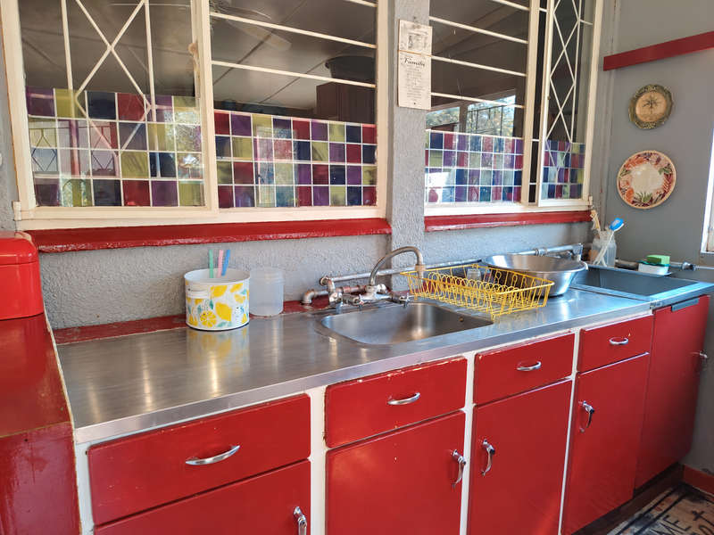 A vintage-style kitchen featuring red metal cabinetry, a stainless steel countertop with integrated sink, and decorative stained-glass window accents.