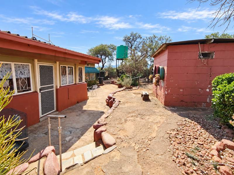 Rear exterior view of the farm property featuring a masonry outbuilding, water tank, and paved courtyard area with stone landscaping.