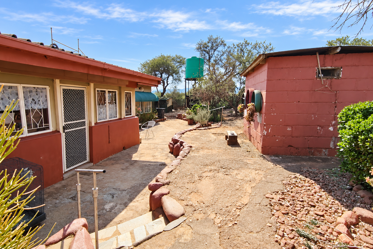 Rear exterior view of the farm property featuring a masonry outbuilding, water tank, and paved courtyard area with stone landscaping.