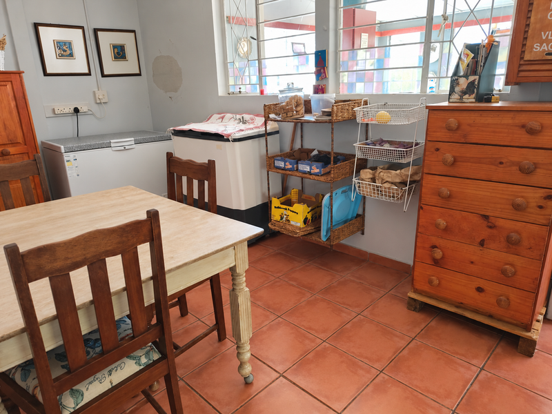 A functional laundry area featuring terracotta tiled flooring, security-barred windows, and wall-mounted electrical points, currently utilized for utility storage.