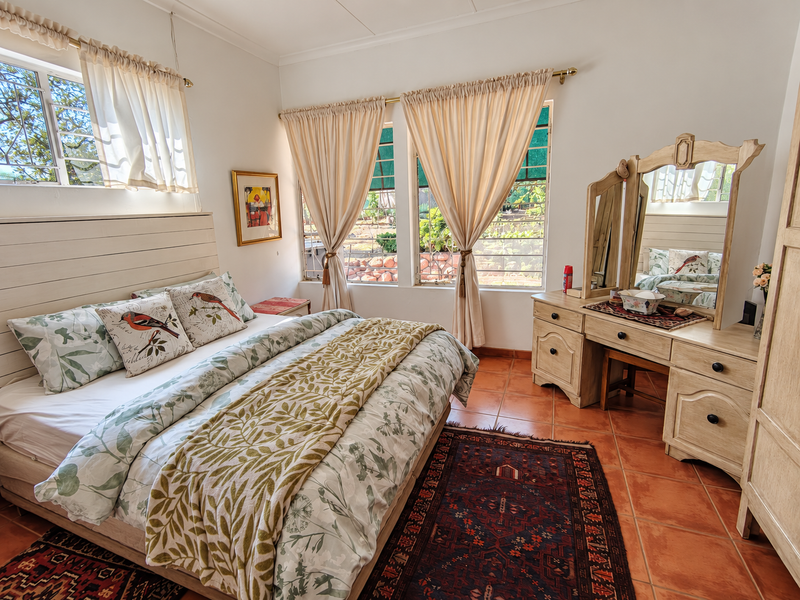 A well-maintained bedroom featuring terracotta floor tiles, a built-in headboard, and large windows that provide ample natural light.
