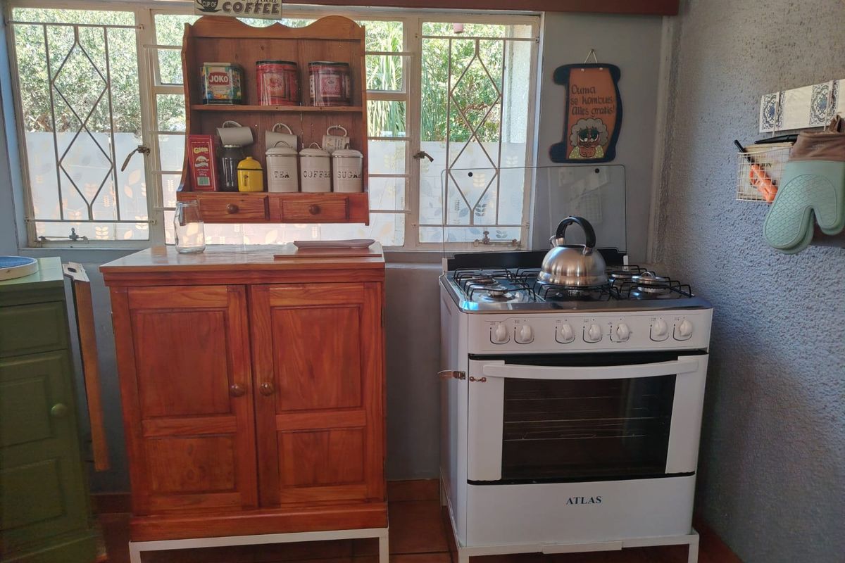A functional kitchen area featuring a freestanding gas stove, tiled flooring, and large windows with security bars.