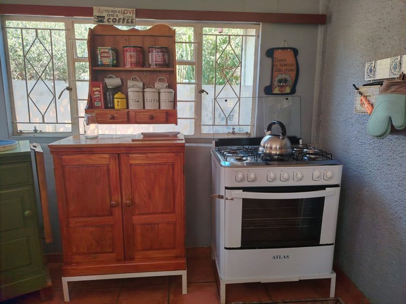 A functional kitchen area featuring a freestanding gas stove, tiled flooring, and large windows with security bars.