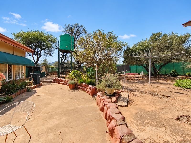 Rear exterior view of the farm property featuring a concrete patio area, stone retaining wall, and a raised water storage tank.