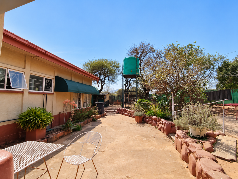 A rear exterior view of the farm property featuring a concrete patio area, stone retaining walls, and an elevated water tank.