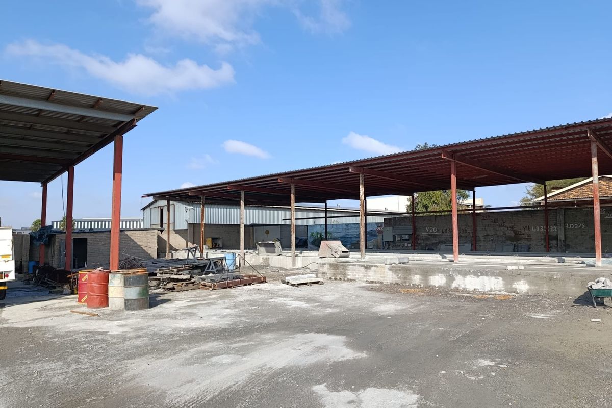 An expansive industrial outdoor area featuring a large steel-framed roof structure over a concrete slab, suitable for storage or workshop operations.