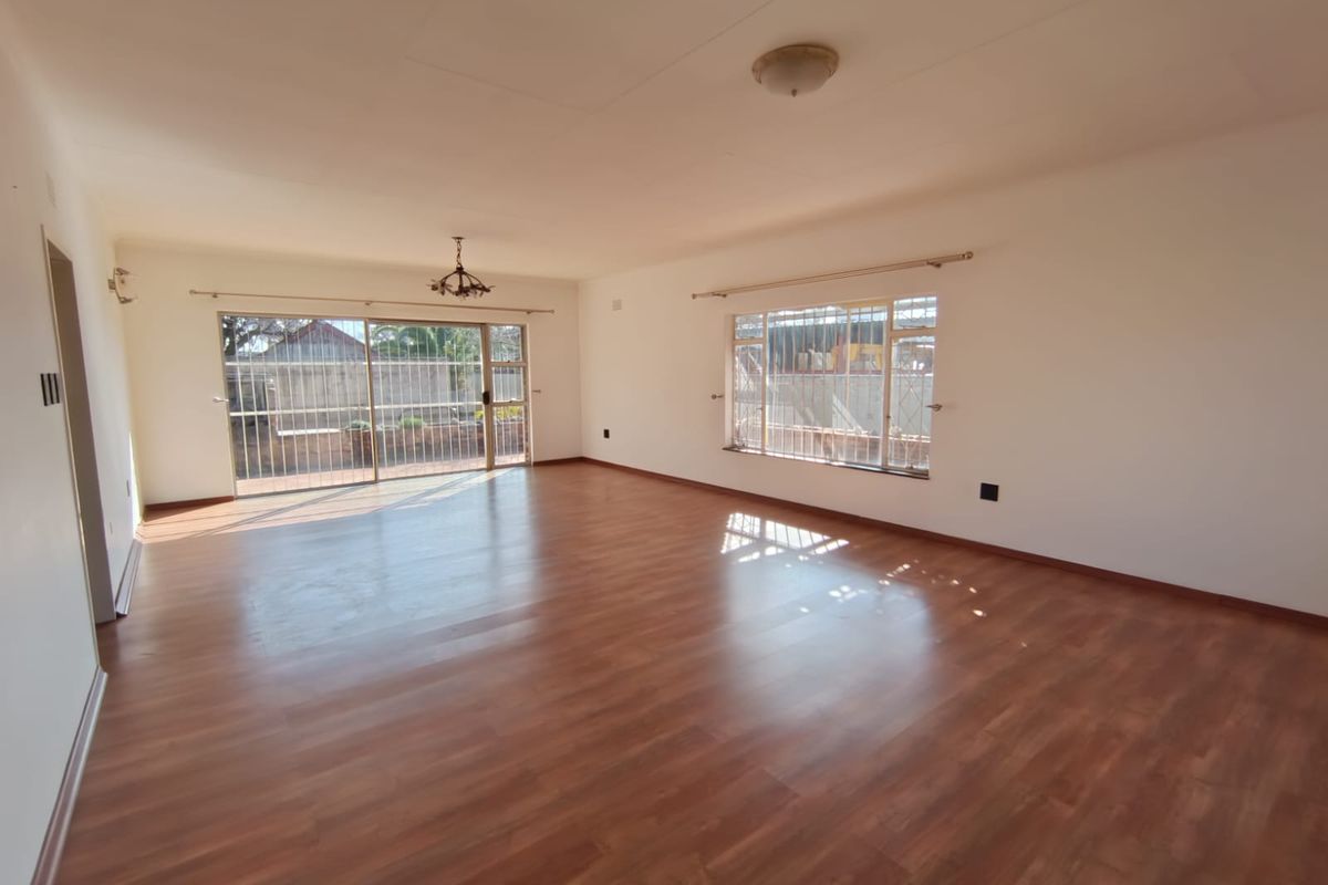 Spacious, empty living area featuring laminate flooring, large windows with security bars, and a sliding glass door leading to the exterior.
