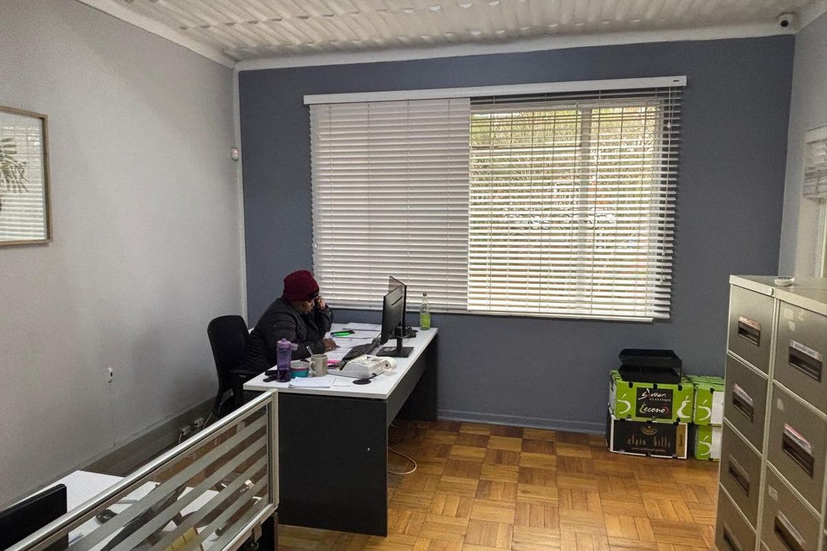 A functional office space featuring parquet flooring, a large window with venetian blinds, and a security camera mounted on the wall.