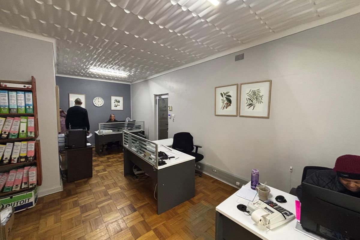 A functional office space featuring parquet flooring and textured ceiling tiles, currently configured with multiple workstations.