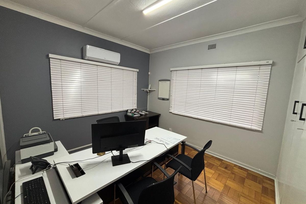 A functional office space featuring parquet flooring, dual-tone walls, venetian blinds, and a wall-mounted air conditioning unit.