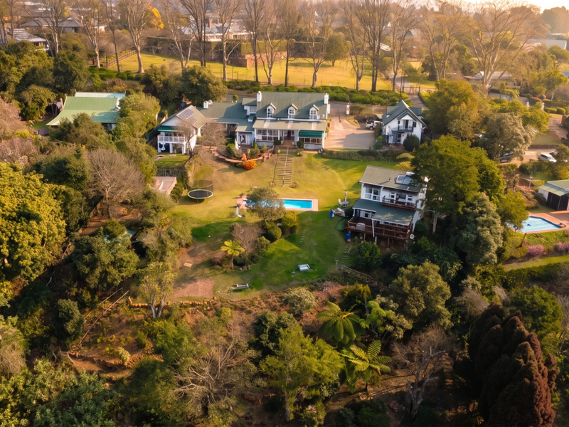 An expansive aerial view of a lush, multi-dwelling guest house property featuring mature trees, landscaped gardens, and multiple swimming pools.