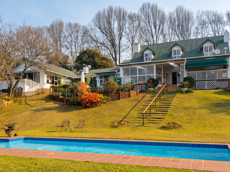 Rear view of the guest house featuring a swimming pool, landscaped lawn, timber staircase, and an enclosed patio area with a metal roof.