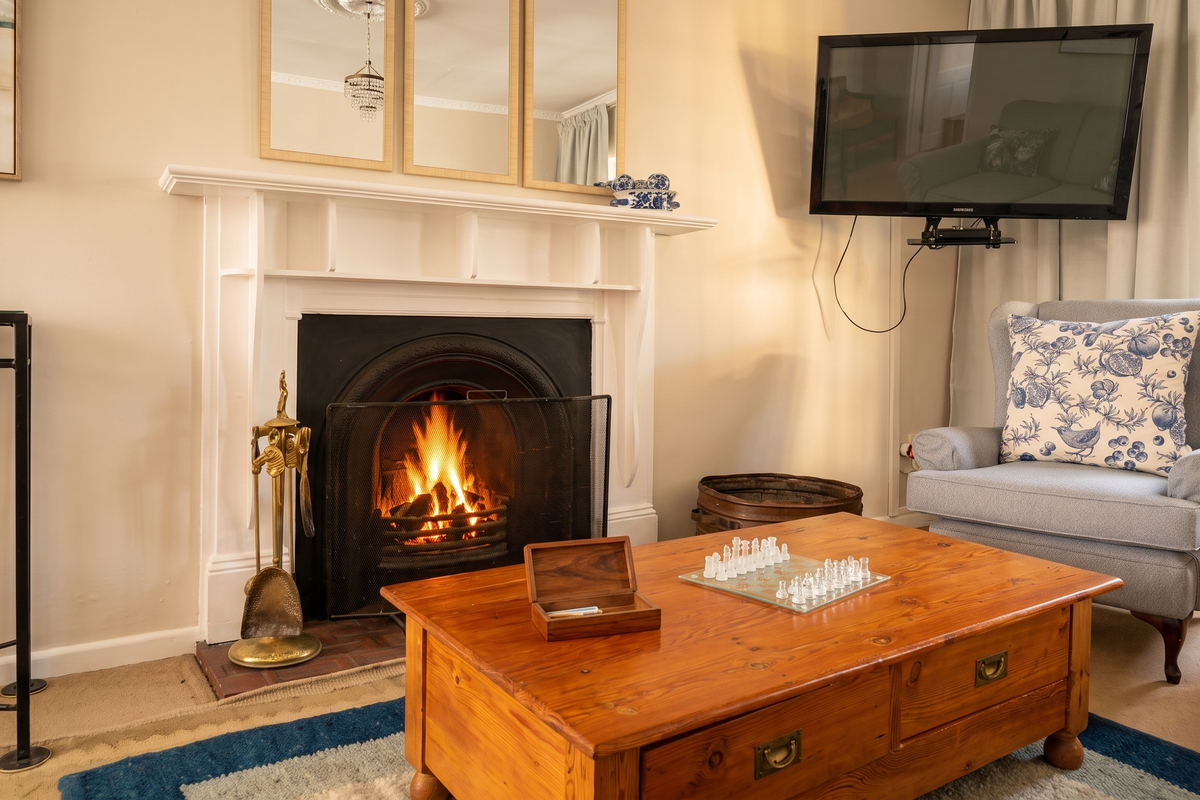 A cozy living room featuring a traditional fireplace with a white mantelpiece, decorative crown molding, and a ceiling rose.