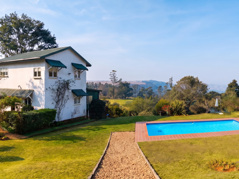 A scenic rear view of the guest house featuring a well-maintained swimming pool, expansive lawn, and beautiful countryside landscape.