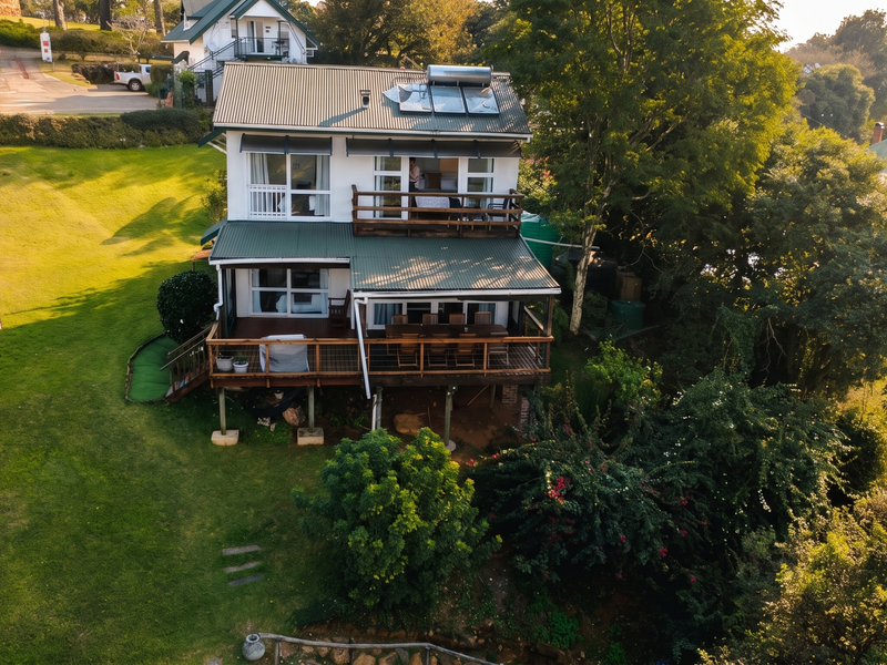 Aerial view of a two-story guest house featuring a timber deck, balcony, corrugated metal roof with solar heating, and a swimming pool in the garden.