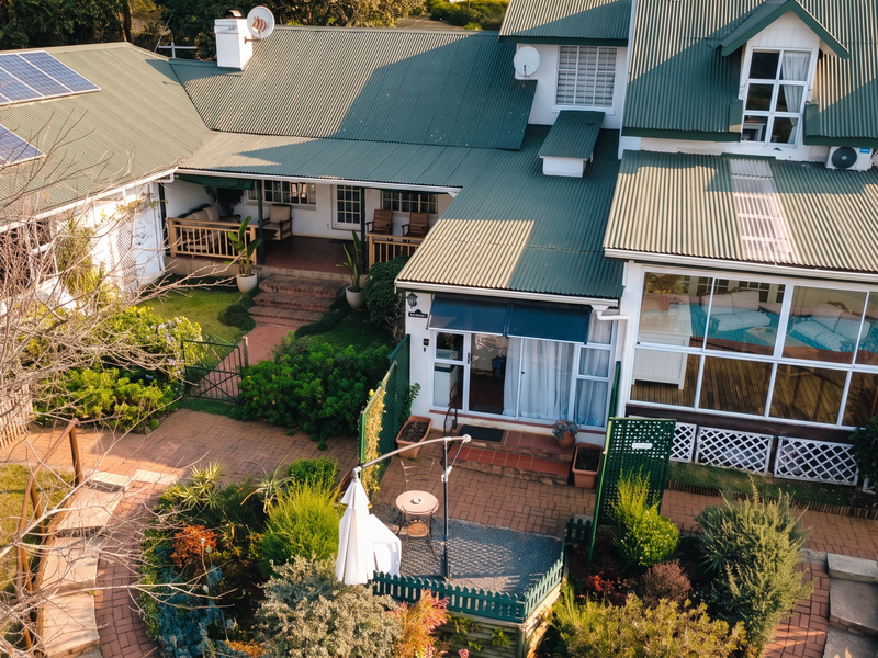 Aerial view of a guest house featuring a green corrugated metal roof, solar panels, paved garden pathways, and an enclosed sunroom area.