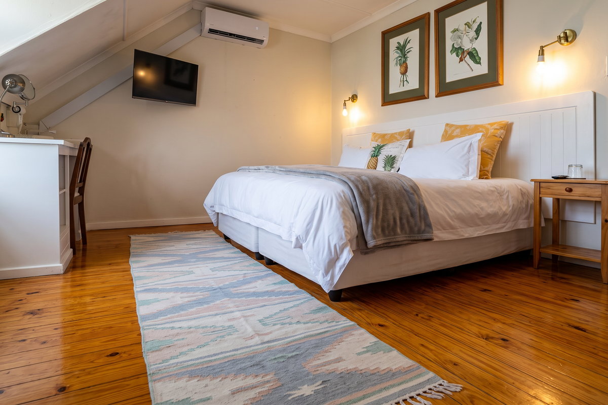 A well-maintained bedroom featuring polished hardwood floors, a built-in headboard, wall-mounted lighting, and an integrated air conditioning unit under a sloped ceiling.