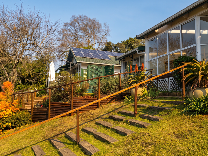 Rear view of the guest house featuring a landscaped garden, timber staircase with metal handrails, and an enclosed patio area with solar panels installed.
