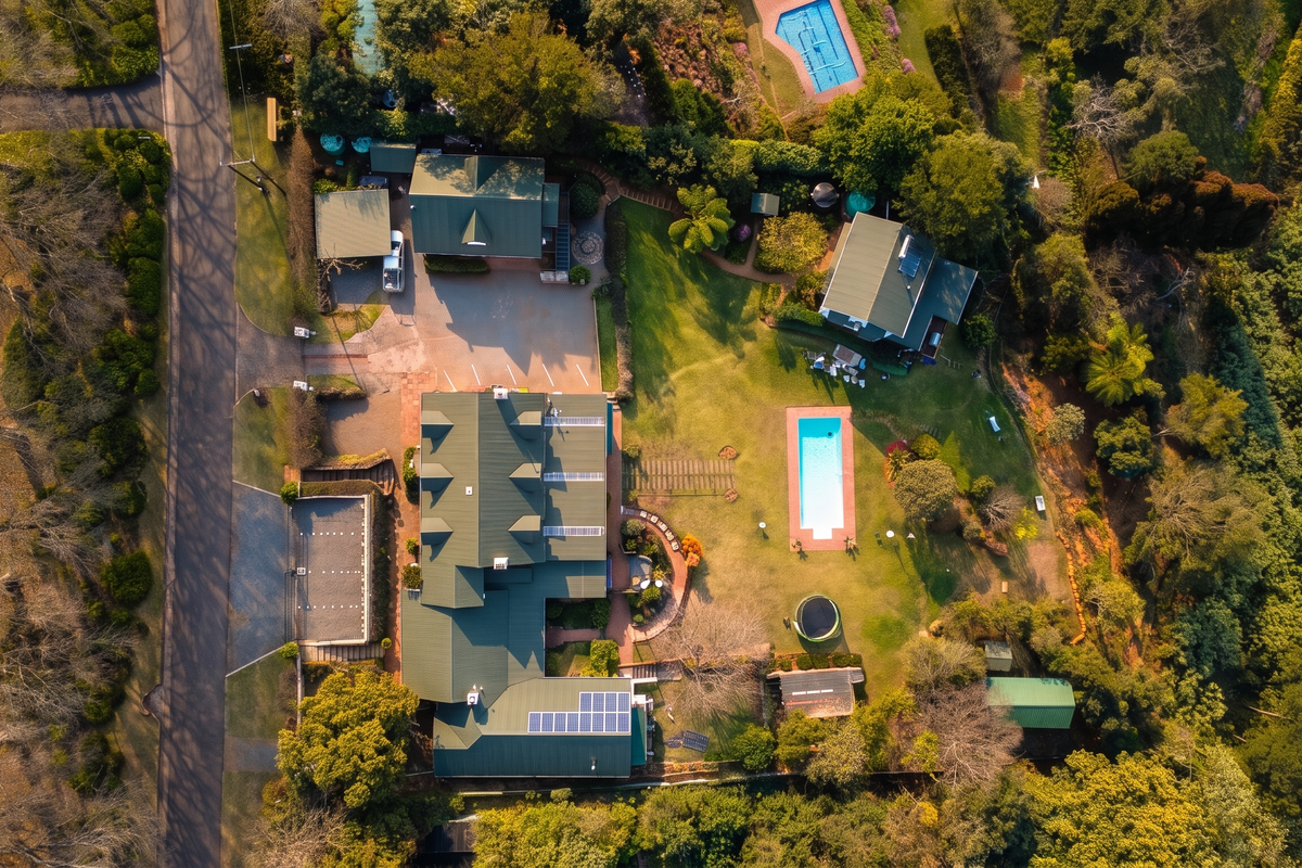 Aerial view of the guest house property featuring multiple buildings, a swimming pool, solar panels, and extensive landscaped grounds.