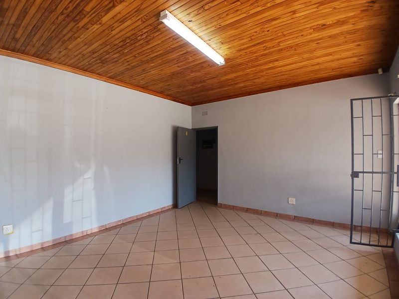 An empty office space featuring ceramic tiled flooring, a timber tongue and groove ceiling, and a security gate at the entrance.