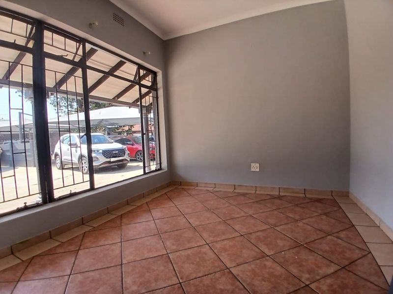 A vacant office space featuring tiled flooring, large windows with security bars, and neutral grey walls, providing a functional workspace.