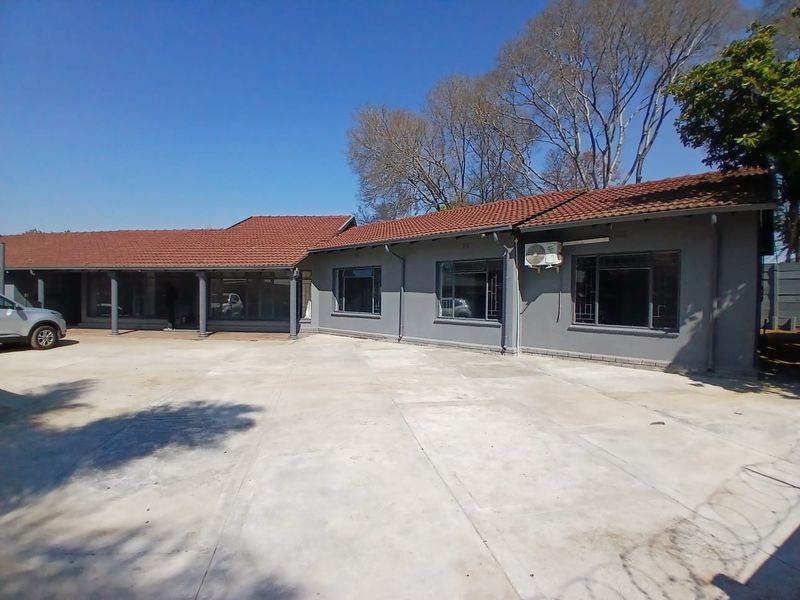 Front exterior view of a single-story office building featuring a large concrete driveway, terracotta tiled roof, and a covered patio area.