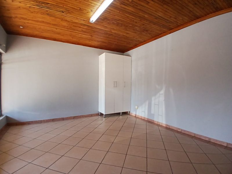 A clean, empty office space featuring warm wooden ceiling paneling, neutral walls, and durable tiled flooring with a built-in storage cupboard.