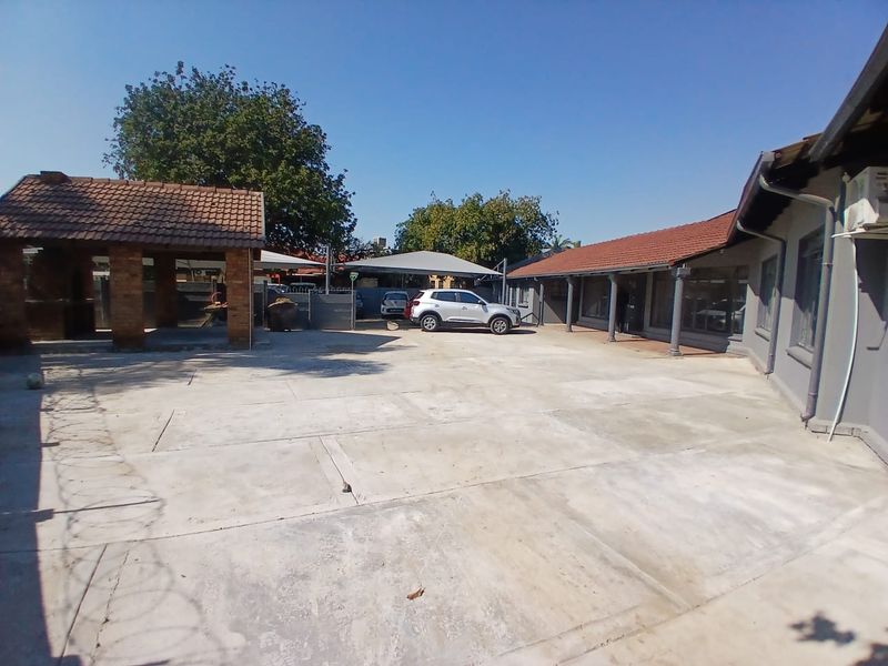 Spacious rear exterior area featuring extensive concrete paving, a covered patio, a brick built-in braai, and shade cloth carport parking.