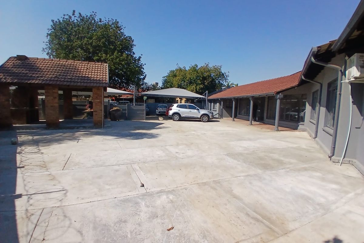 Spacious rear exterior area featuring extensive concrete paving, a covered patio, a brick built-in braai, and shade cloth carport parking.