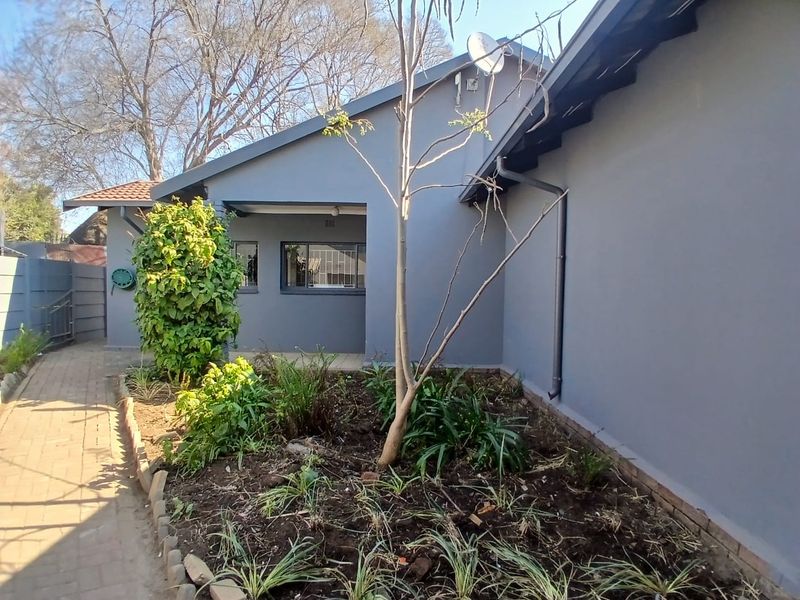Rear exterior view of the office building featuring a paved walkway, landscaped garden bed, and grey painted facade with security bars on windows.
