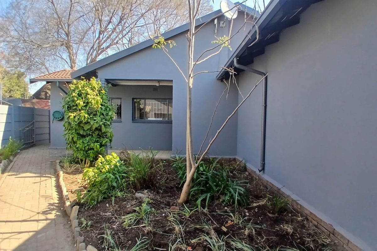 Rear exterior view of the office building featuring a paved walkway, landscaped garden bed, and grey painted facade with security bars on windows.