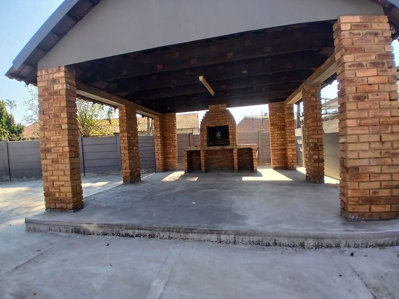 Covered outdoor patio area featuring exposed brick pillars, a built-in brick braai, and concrete flooring, ideal for an entertainment space.