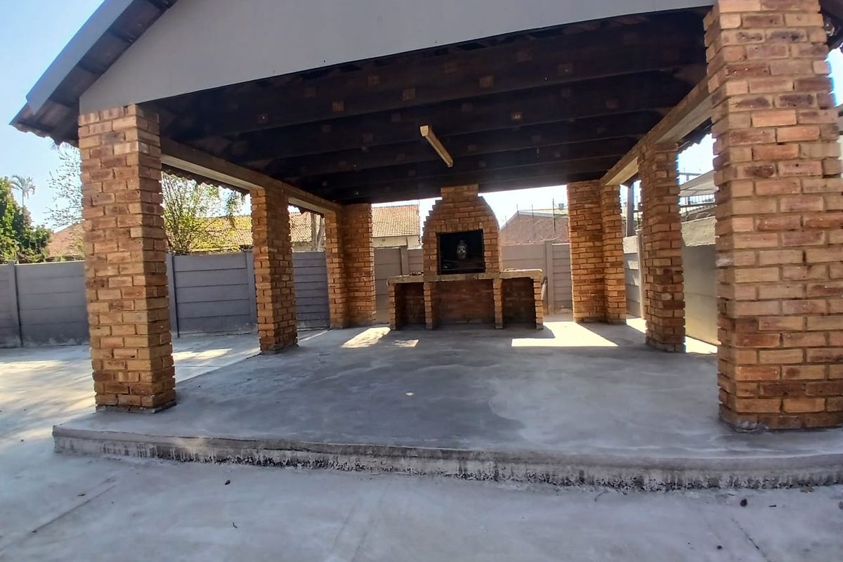Covered outdoor patio area featuring exposed brick pillars, a built-in brick braai, and concrete flooring, ideal for an entertainment space.