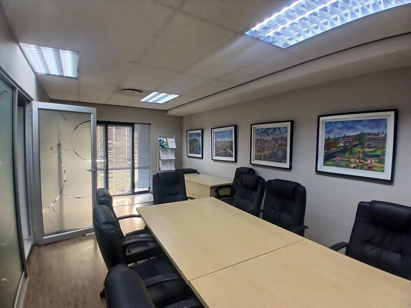A professional office meeting room featuring a suspended ceiling, recessed lighting, laminate flooring, and a modern frosted glass entrance door.