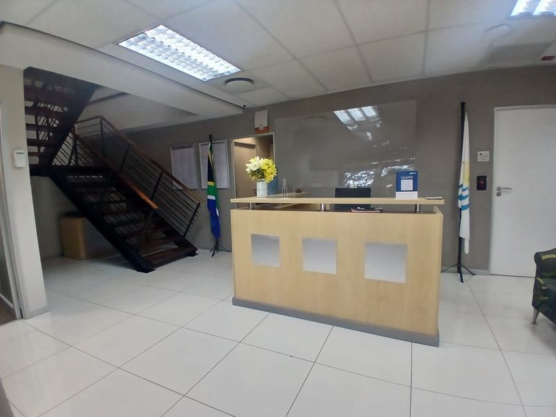 Professional office reception area featuring a built-in reception desk, modern staircase, tiled flooring, and recessed ceiling lighting.