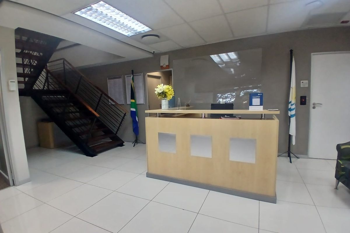 Professional office reception area featuring a built-in reception desk, modern staircase, tiled flooring, and recessed ceiling lighting.